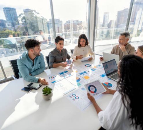 Multi racial group of people working with Paperwork on a board room table at a business presentation or seminar. The documents have financial or marketing figures, graphs and charts on them. There is a laptop and digital tablet  on the table. Multi ethnic group including Caucasian and African American